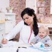 Mother with baby in the kitchen working with documents and speaks by phone