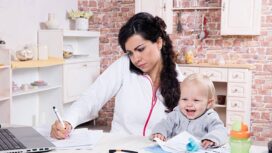 Mother with baby in the kitchen working with documents and speaks by phone