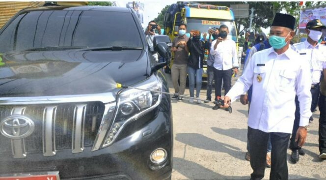
					Bupati OKU Timur Kholid Mawardi saat menyemprot disinfektan di kendaraan dinasnya (Dok. Humas OKUT)