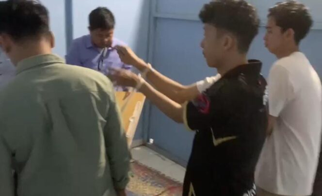 
Polisi saat menggerebek lokasi yang diduga tempat digunakan terdduga (pria yang mengenakan baju hitam) melakukan promosi judi online. Foto : Istimewa