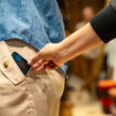 Close-up on a thief stealing a cell phone of a customer at a shopping store - pickpocketing concepts