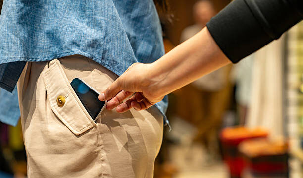 Close-up on a thief stealing a cell phone of a customer at a shopping store - pickpocketing concepts